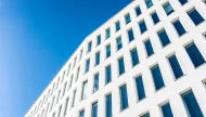 A low-angle photograph of a modern white building with a repeating pattern of rectangular windows set against a clear, deep blue sky.