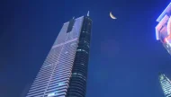A low-angle nighttime photograph of the illuminated Shun Hing Square skyscraper in Shenzhen, China, with a crescent moon visible in the deep blue twilight sky.