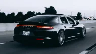 A sleek black Porsche Panamera Turbo captured in a motion shot as it drives on a highway at dusk, with its distinctive red LED taillight bar illuminated.