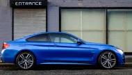A vibrant Estoril Blue BMW 4 Series coupe parked on an urban street in front of a gray brick building with an 'ENTRANCE' sign.
