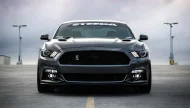 An aggressively styled, dark gray Steeda Ford Mustang parked head-on in a rooftop parking lot under a dramatic, cloudy sky.