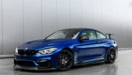 A stunning San Marino Blue BMW M4 coupe with a carbon fiber roof and aero parts, covered in water droplets and parked inside a modern garage.