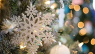 A beautiful close-up of a sparkling silver glitter snowflake ornament hanging on a Christmas tree, with warm, out-of-focus lights creating a magical bokeh effect.