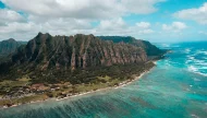 Stunning aerial panorama of the Koʻolau Mountain Range on the coast of Oahu, Hawaii, showing the dramatic green ridges meeting the vibrant turquoise Pacific Ocean.