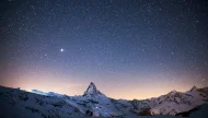 A breathtaking night-time photograph of the iconic Matterhorn in the Swiss Alps, surrounded by a snow-covered landscape under a crystal-clear, star-filled sky.